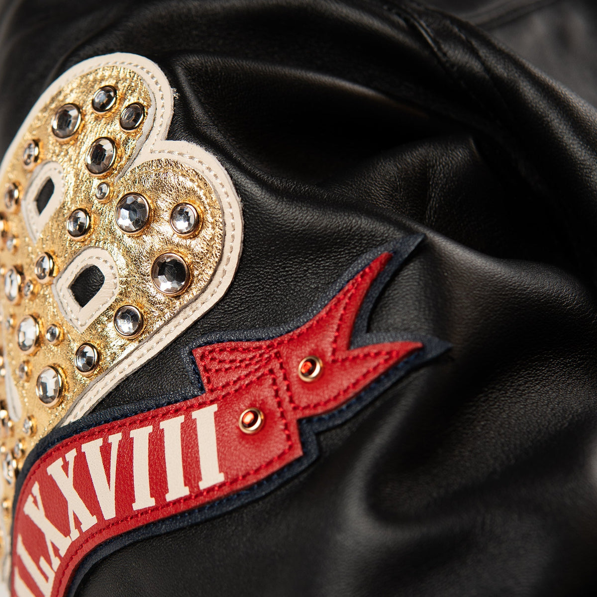 Front view of a black leather anniversary jacket with a decorated chest crest, gold-tone zipper and two angled pockets