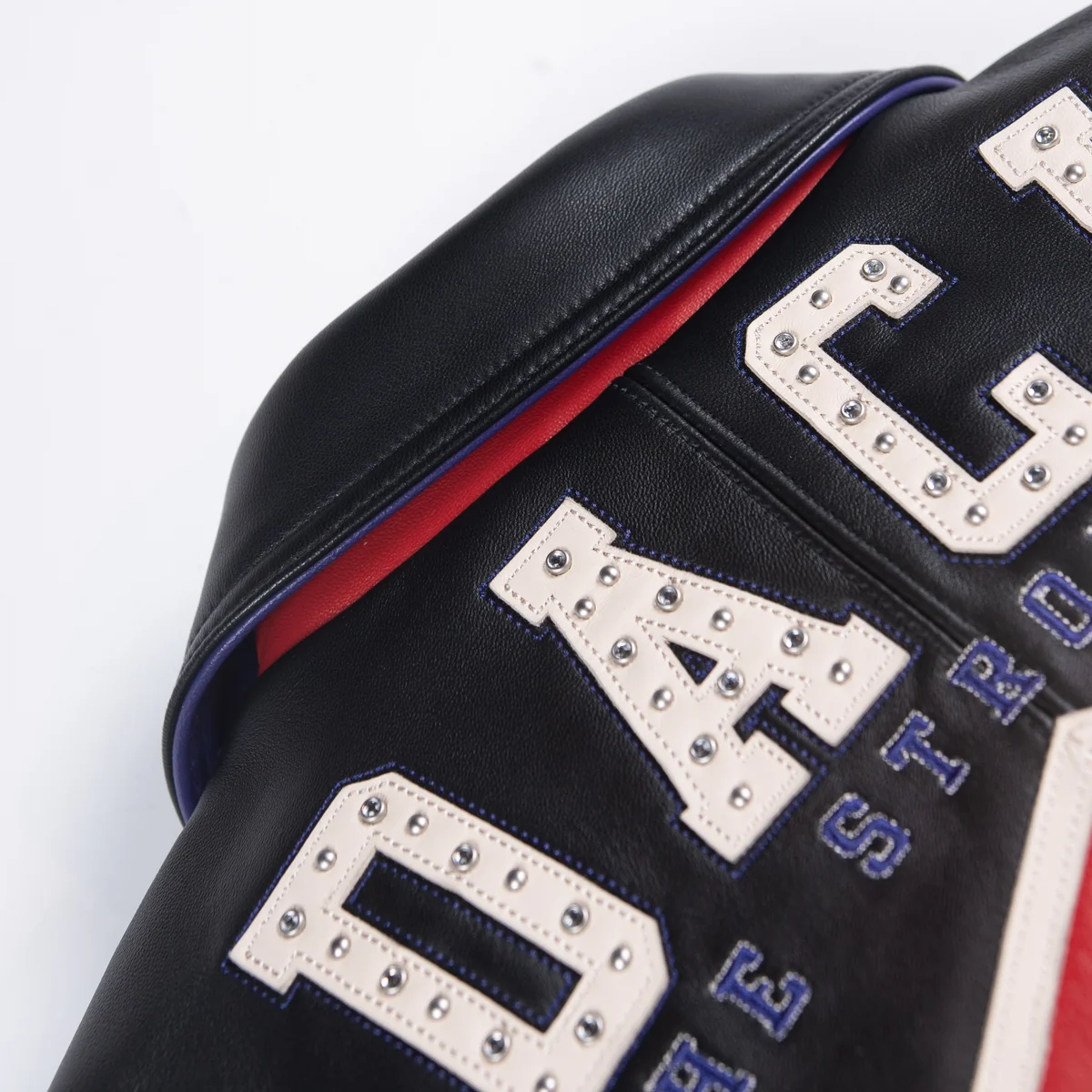 Close view of the black leather jacket's upper back showing studded cream lettering, purple stitching and contrasting collar piping.