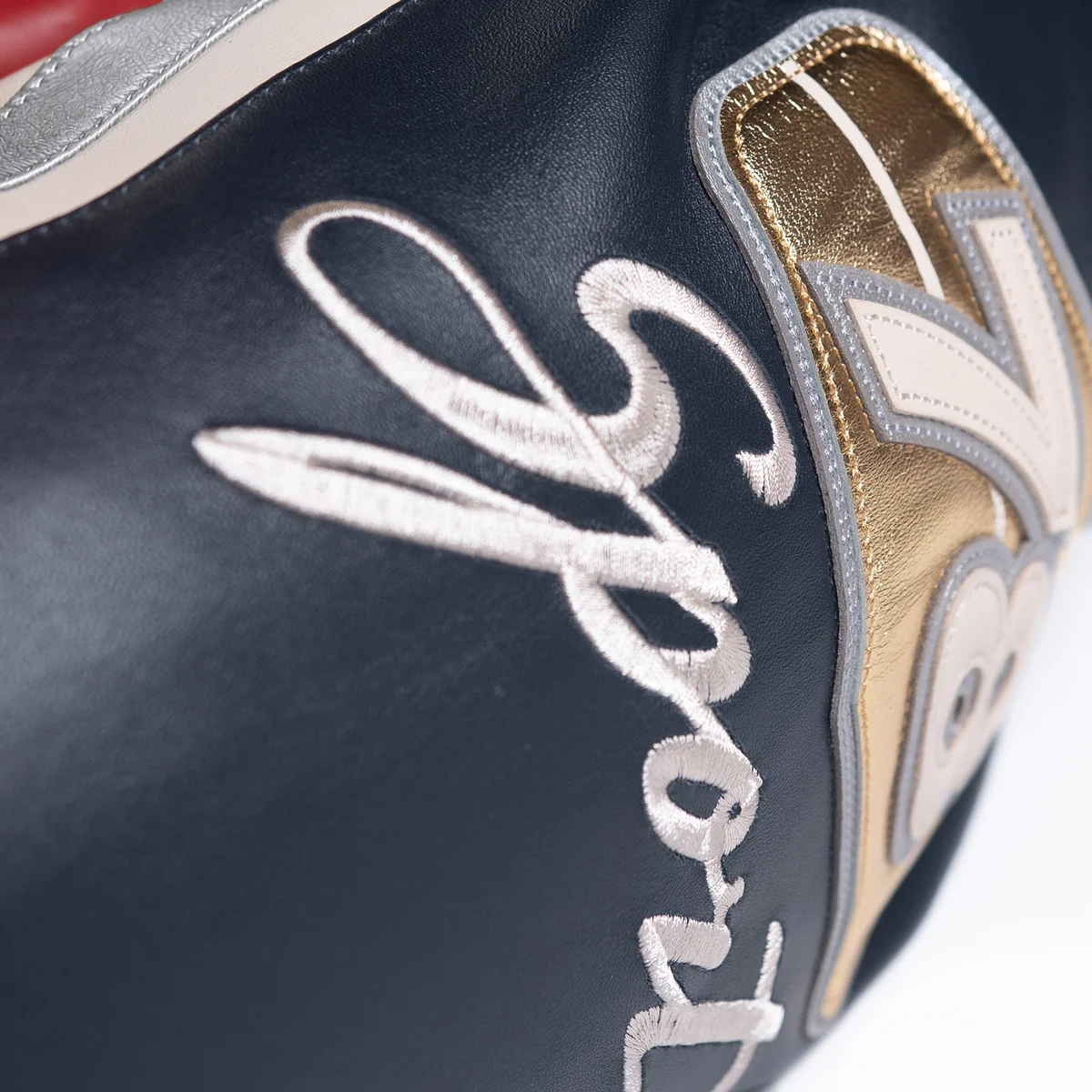 Close view of cream Sport embroidery on the black jacket sleeve beside a metallic gold and silver patch with stitched applique details.