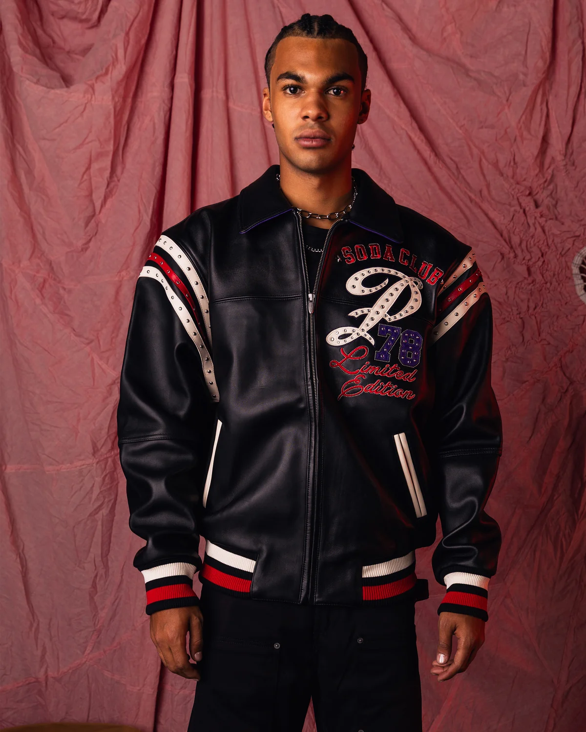 Model wearing a black leather Soda Club 78 jacket with cream and red accents, studded shoulder stripes, pointed collar and striped cuffs.